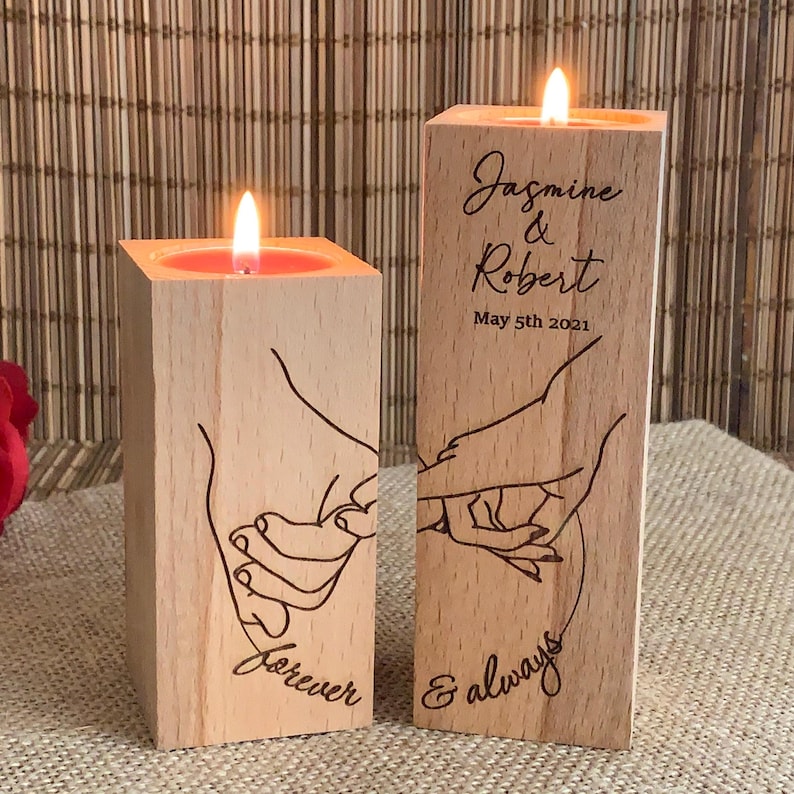 May include: Two wooden candle holders with a hand-drawn design of two hands holding each other. The candle holder on the left says "forever" and the candle holder on the right says "& always". The candle holder on the right also has the text "Jasmine & Robert May 5th 2021".