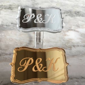 May include: Two acrylic signs with the initials "P&K" engraved on them. The top sign is clear and the bottom sign is gold.