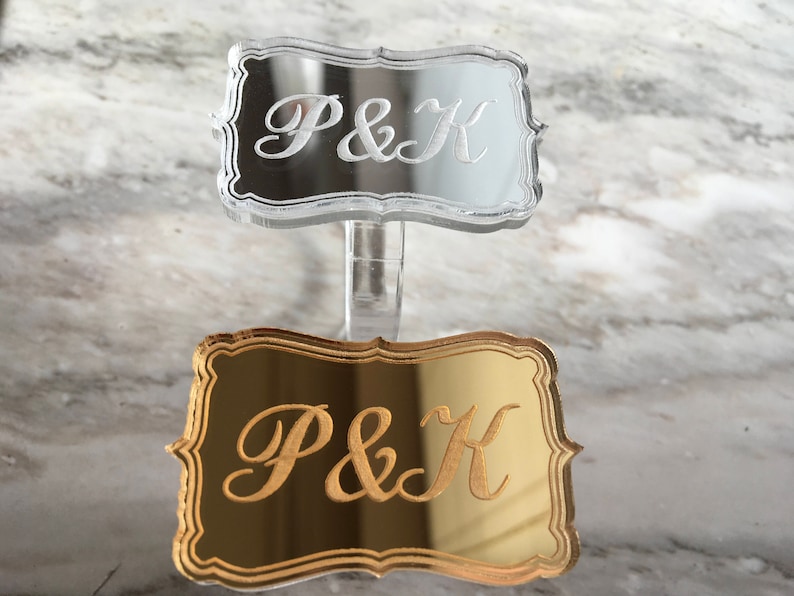 May include: Two acrylic signs with the initials "P&K" engraved on them. The top sign is clear and the bottom sign is gold.