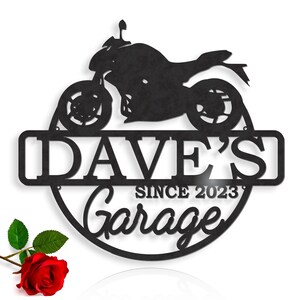 K&ouml;nnte beinhalten: Schwarzes Metallschild mit einer Motorradsilhouette, dem Text "Dave's Garage Since 2023" und einem dekorativen Rand.