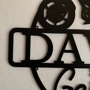 K&ouml;nnte beinhalten: Schwarzes Metallschild mit dem Namen "DAVE" und einem stilisierten Autodesign. Das Schild hat einen Used-Look und ist perfekt f&uuml;r eine Garage oder einen M&auml;nnerraum.