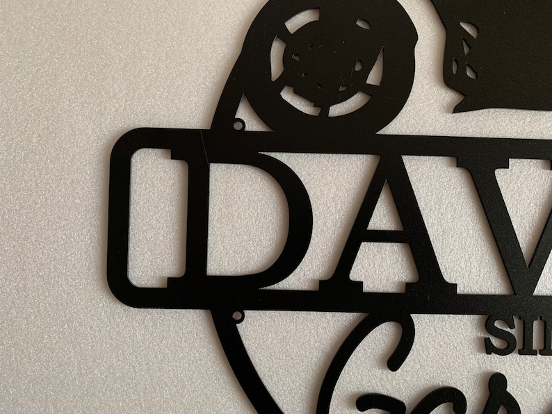 K&ouml;nnte beinhalten: Schwarzes Metallschild mit dem Namen "DAVE" und einem stilisierten Autodesign. Das Schild hat einen Used-Look und ist perfekt f&uuml;r eine Garage oder einen M&auml;nnerraum.