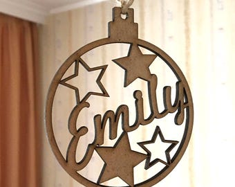 Puede incluir: Un adorno de Navidad de madera con forma de bola con el nombre "Emily" recortado y cuatro estrellas.