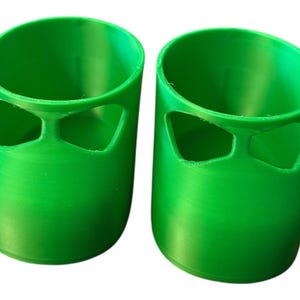 May include: Two bright green, cylindrical objects with a unique design. Each has a rounded top and a distinctive cutout near the top, creating an interesting visual element. The objects are made of a solid, smooth material.