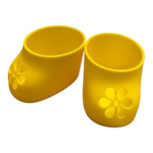 May include: Two bright yellow, open-topped, shoe-shaped containers. Each container has a flower-shaped cutout on the front. The containers are made of a smooth, solid material and are set against a white background.