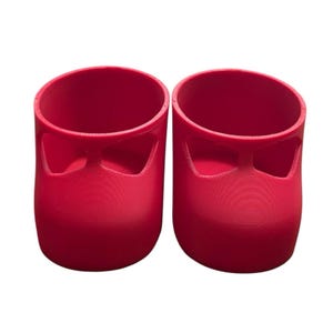May include: Two red, cylindrical objects with a curved top and a cutout design. The objects are side-by-side, and appear to be made of a solid material. The colour is a vibrant, solid red.