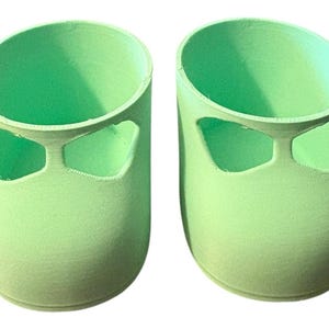 May include: Two light green, cylindrical objects with a rounded top and a cut-out design on the side. The objects are side by side, and the background is white.