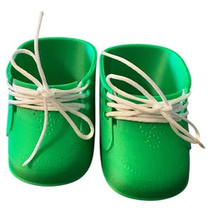 May include: A pair of vibrant green baby shoes with white laces tied in bows. The shoes have a classic sneaker design, with a rounded toe and a textured surface. The laces are thick and white.