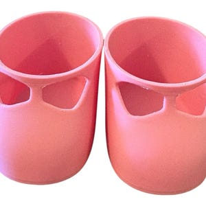 Könnte beinhalten: Ein Paar rosa Puppenschuhe. Jeder Schuh hat eine abgerundete Spitze und ein Ausschnittdesign über der Spitze. Die Schuhe bestehen aus einem festen, glatten Material und sind in einem hellen Rosaton gehalten.