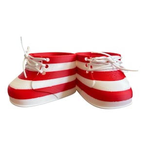 May include: A pair of red and white striped baby shoes with white laces. The shoes have a rounded toe and a low-top design. The red stripes are horizontal and evenly spaced across the shoe.