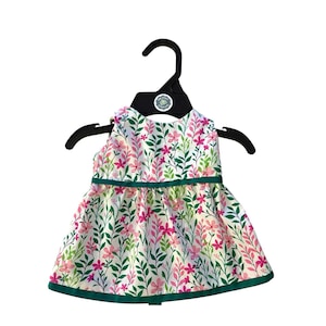 May include: A sleeveless floral print dress with a white background, adorned with pink flowers and green leaves. The dress has a green trim and is hanging on a black hanger.