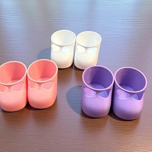 Może przedstawiać: Sześć małych pojemników w kształcie butów w różnych kolorach. Dwa są białe, dwa różowe i dwa fioletowe. Każdy ma zaokrągloną górę i wycięty wzór z przodu.