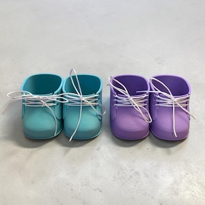 May include: Two pairs of small, colorful shoes. One pair is turquoise, the other is purple. Each shoe has white laces tied in a bow. The shoes are likely for a baby or small child.