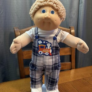 以下が含まれることがあります： 黒い持ち手と「But First, Coffee」のテキストが黒い太字で書かれた白いセラミックマグ。マグカップはぼやけた背景に置かれ、居心地の良い環境を暗示しています。