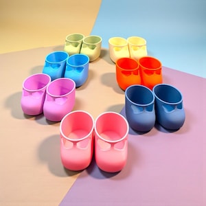 Könnte beinhalten: Eine Sammlung farbenfroher Miniaturschuhe in verschiedenen Rosa-, Blau-, Gelb- und Orangetönen. Die Schuhe haben eine runde Spitze und einen bogenförmigen Ausschnitt auf der Oberseite. Der Hintergrund ist eine Mischung aus Pastellfarben.