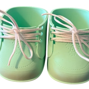 May include: A pair of mint green baby shoes with white laces. The shoes have a classic sneaker design with a rounded toe and a textured surface. The laces are tied in a bow.