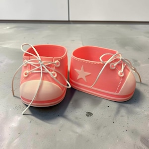 May include: A pair of coral pink low-top sneakers with white laces, a white rubber toe cap, and a white star emblem on the side. The shoes feature white eyelets and a white sole with a thin coral pink stripe running along the base of the shoe.