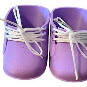 May include: A pair of lavender-colored baby sneakers with white laces. The shoes have a classic sneaker design with a rounded toe and a textured surface. The laces are tied in a bow.