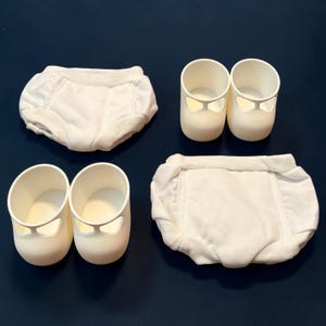 May include: A set of baby items, including two pairs of white Mary Jane style shoes and two pairs of white cloth diapers. The shoes have a rounded toe and a strap across the top. The diapers are made of a soft, absorbent material.