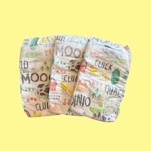 May include: Three white baby diapers with farm animal illustrations and the words "MOO", "CLUCK", "OINK", and "QUACK". The diapers have a colorful design with images of cows, chickens, and other farm elements.