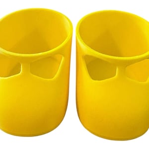 May include: Two bright yellow, cylindrical containers with a unique design. Each container has a rounded top and a distinctive cutout resembling a stylized face. The containers are made of a solid, opaque material.