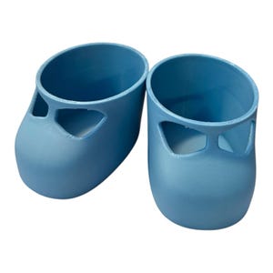 May include: A pair of light blue baby shoes. Each shoe has a rounded toe and a cutout design on the top. The shoes are made of a solid, smooth material and are designed to be worn by infants.