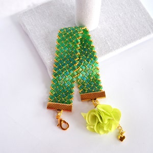 Peut inclure: Un bracelet en perles vertes avec des accents dorés et un charme de fleur en tissu vert attaché à une chaîne dorée.