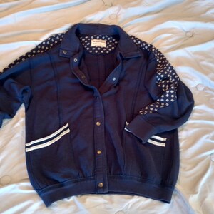May include: Navy blue jacket with white polka dots on the sleeves and a white stripe detail on the pockets. The jacket has a button-up front and a collared neckline. The jacket is made of a soft material.