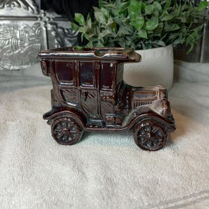 Könnte beinhalten: Ein brauner Keramik-Aschenbecher in Form eines Oldtimers. Das Vintage-Auto hat detaillierte Merkmale, darunter Räder, Türen und ein Dach. Der Aschenbecher ist ein dekorativer Artikel mit glänzendem Finish, ideal für Sammler.