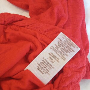 Puede incluir: Primer plano de una prenda roja brillante y texturizada. Se ve una etiqueta blanca con texto negro, que incluye instrucciones de lavado en franc&eacute;s e ingl&eacute;s, y el texto "FABRICADO NA INDIA".