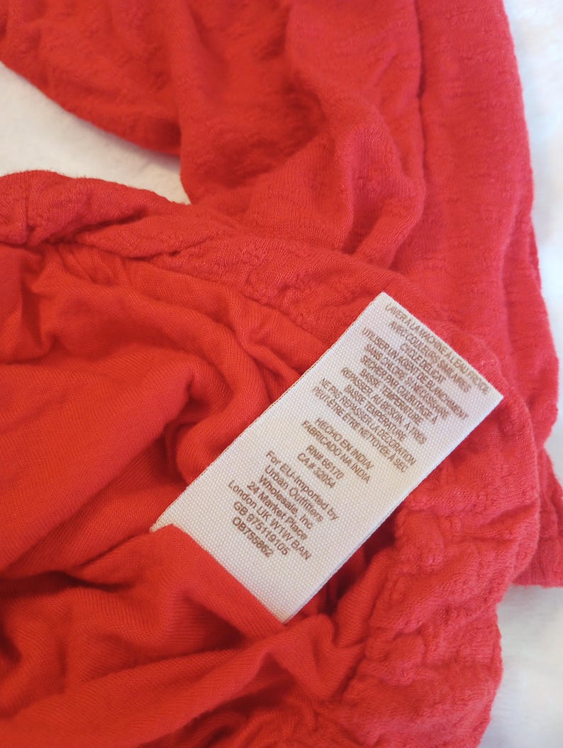 Puede incluir: Primer plano de una prenda roja brillante y texturizada. Se ve una etiqueta blanca con texto negro, que incluye instrucciones de lavado en franc&eacute;s e ingl&eacute;s, y el texto "FABRICADO NA INDIA".