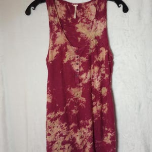 May include: A burgundy and beige tie-dye sleeveless top with a scoop neck and button-up placket, hanging on a black hanger. The fabric appears to be a soft, lightweight material. The top is a casual style.