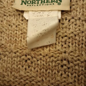 May include: A beige knitted sweater with a brown label that says "Northern Reflections" and features a pair of loons. The label also includes care instructions.