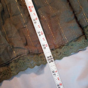 K&ouml;nnte beinhalten: Olivgr&uuml;ner Stoff mit goldenen Metallic-Streifen und einer Spitzenborte. Ein Ma&szlig;band zeigt, dass der Stoff etwa 76 bis 99 cm lang ist.