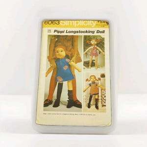 Może przedstawiać: Vintage wz&oacute;r szycia Simplicity dla lalki Pippi Langstrumpf. Wz&oacute;r przedstawia lalkę w niebieskiej sukience z łatkami, czarnych pończochach i rudych warkoczach. Opakowanie znajduje się w przezroczystym plastikowym etui.