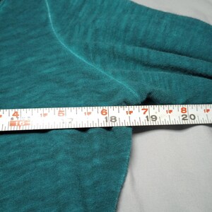 May include: Teal long-sleeve shirt with a crew neck. The shirt is made of a soft, textured fabric. A ruler is placed across the shirt, measuring approximately 6 inches.