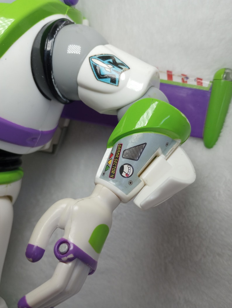 May include: A plastic action figure arm featuring a white, green, and purple color scheme. The upper arm displays a blue and white rocket emblem, while the forearm includes a graphic label with the text GAMMA SECTOR 4 and a circular gauge.