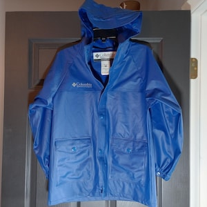Könnte beinhalten: Ein blauer Kapuzenregenmantel mit Reißverschluss und Knopfleiste. Die Jacke hat zwei große Taschen und das Columbia-Logo ist auf der Vorderseite aufgedruckt.