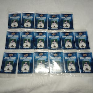 May include: Seventeen sealed packs of Upper Deck hockey cards. Each pack has a blue and white design with the words "HOCKEY CARDS" at the top. The packs feature a player image and are arranged on a white surface.