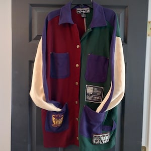May include: A multi-colored jacket with a white, cream, red, green, and purple color scheme. The jacket has a button-up front and a patch pocket on the left side. The jacket has a variety of patches and designs on the front.