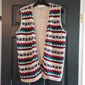 May include: A beige knitted vest with a geometric pattern in shades of red, green, and white. The vest has a V-neck and is sleeveless.