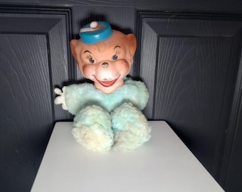 May include: A vintage plush toy monkey wearing a blue and white hat. The monkey has a light blue and white fuzzy body and a smiling face.