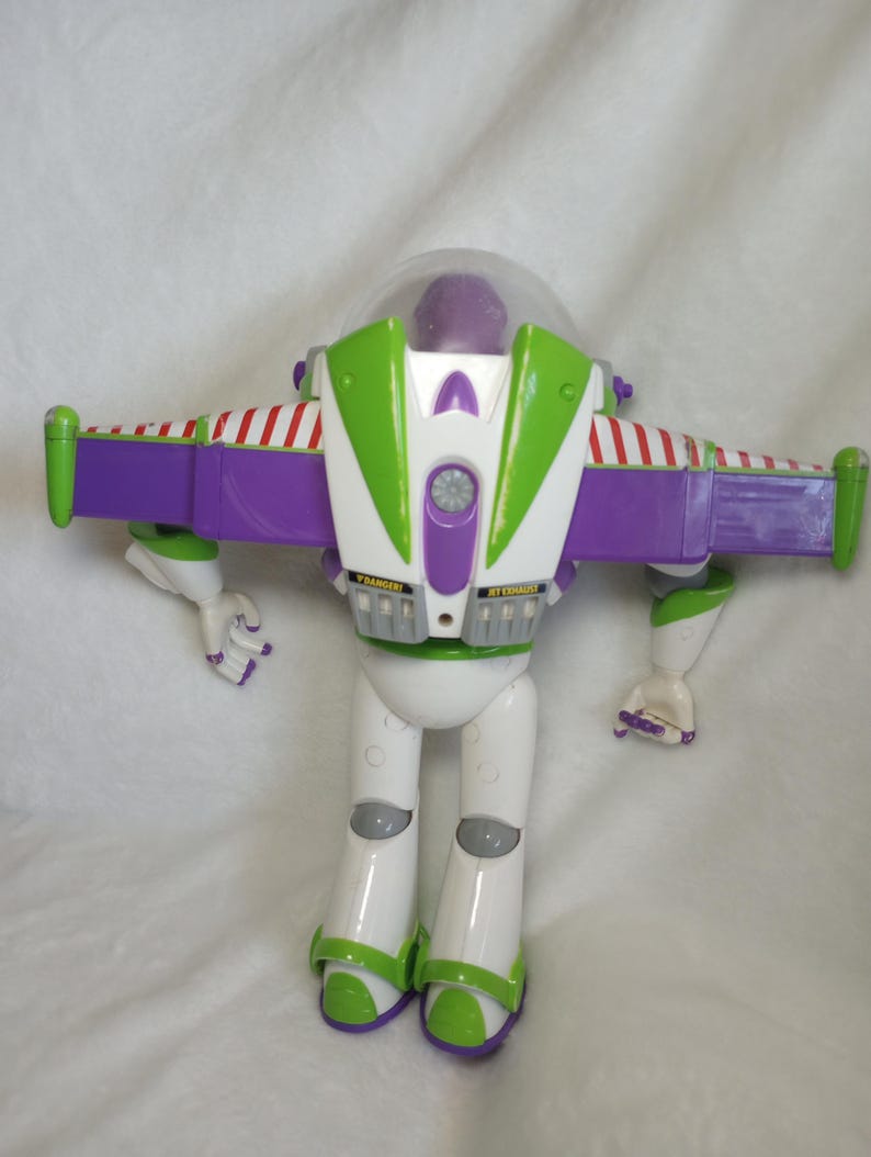 May include: A plastic action figure of a space ranger character with a purple head, white body, and green accents. The figure features extended purple wings with red and white striped detailing, a clear dome helmet, and labels reading DANGER and JET EXHAUST.