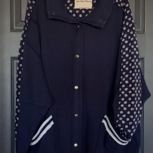 May include: Navy blue jacket with a button-up front, featuring white striped accents on the pockets and sleeves with a white polka dot pattern. The interior lining and sleeves have a white polka dot pattern. The jacket has a label that says "We The Free".