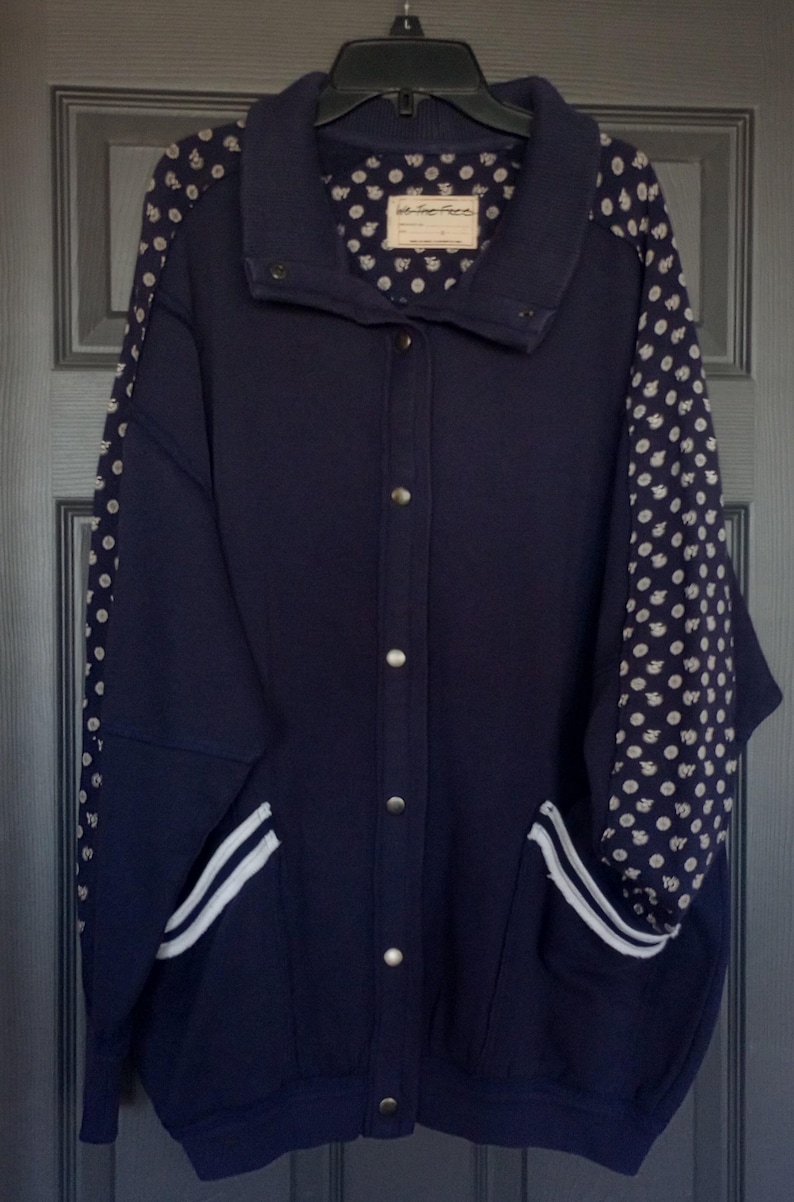 May include: Navy blue jacket with a button-up front, featuring white striped accents on the pockets and sleeves with a white polka dot pattern. The interior lining and sleeves have a white polka dot pattern. The jacket has a label that says "We The Free".