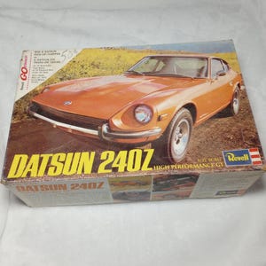 May include: A vintage Revell model kit box featuring an orange Datsun 240Z car. The box has the text "DATSUN 240Z" in large yellow letters, with "HIGH PERFORMANCE GT" below. The box also includes the text "1/25 SCALE".