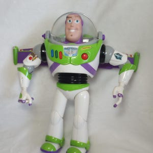 May include: A plastic action figure of a space ranger character with a clear dome helmet, white, green, and purple suit, and black waist. The chest features a badge with the text SPACE RANGER and LIGHTYEAR, along with red, blue, and green buttons.