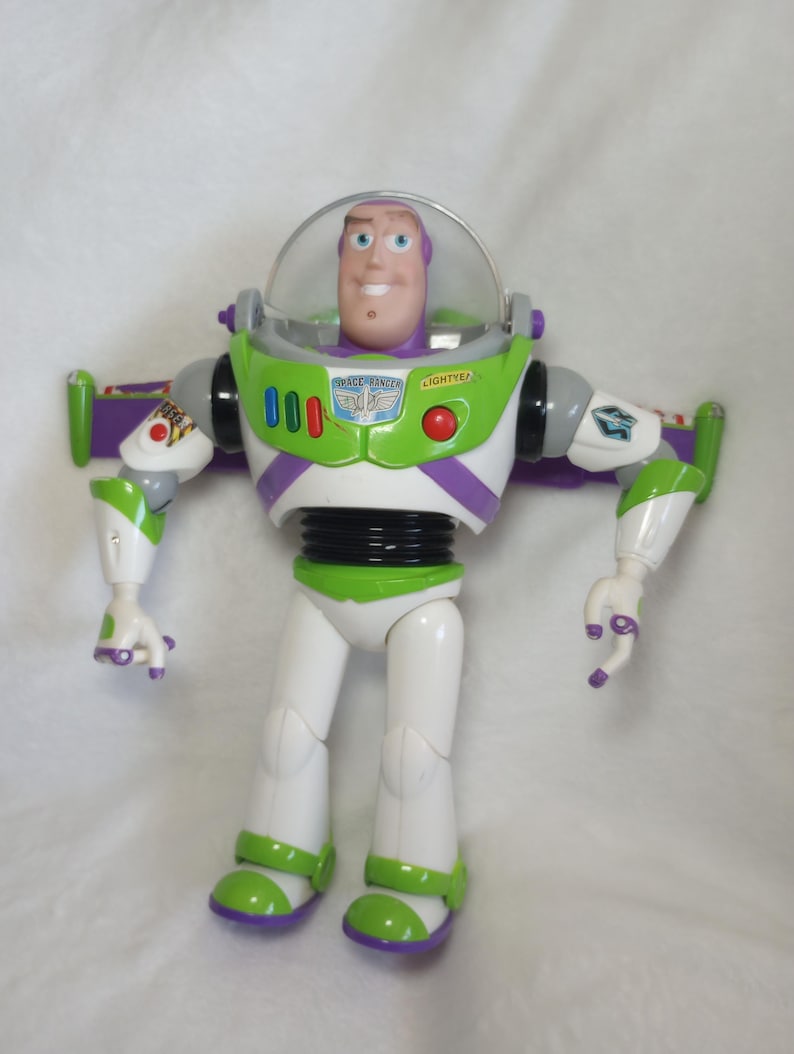 May include: A plastic action figure of a space ranger character with a clear dome helmet, white, green, and purple suit, and black waist. The chest features a badge with the text SPACE RANGER and LIGHTYEAR, along with red, blue, and green buttons.