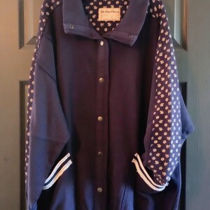 May include: A navy blue jacket with a button-up front, featuring white polka dot patterned sleeves and a ribbed collar. The jacket has a label that reads "We The Free". The jacket has two white stripes on the cuffs.