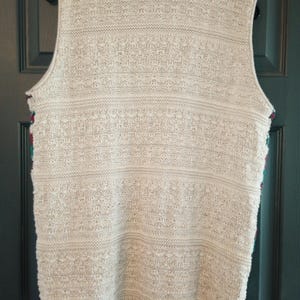 May include: A cream-colored knitted vest with a textured pattern. The vest has a V-neck and sleeveless design.